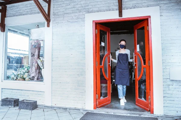 Florist woman wearing apron and face mask standing open the door flower shop — Stock Photo, Image