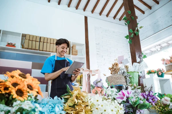 Çiçekçide çalışan mutlu genç girişimci. Önlük giymiş, gülümsüyor. — Stok fotoğraf