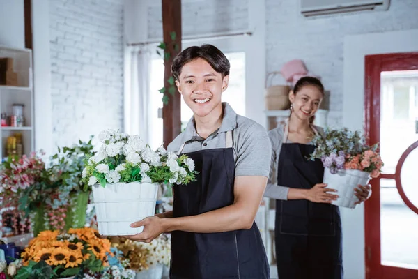 Jovem florista feliz vestindo avental segurando flor balde sorrindo olhando para a câmera. trabalhando na loja de flores — Fotografia de Stock