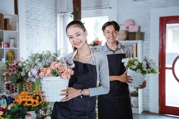 Feliz jovem florista feminina vestindo avental segurando flor balde sorrindo olhando para a câmera. trabalhando na loja de flores — Fotografia de Stock