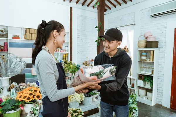 Sorridente jovem lojista vestindo um avental. manutenção de compradores de flores de flanela masculina — Fotografia de Stock