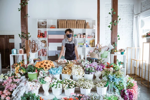 florist man wearing face mask standing behind a flower bouquet