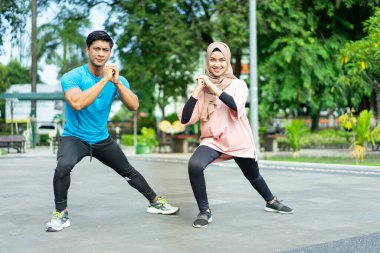 Spor kıyafetleri içinde müslüman çiftler egzersiz yapmadan önce bacakları ısıtmaya çalışıyorlar.