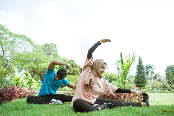 Seorang pemuda dan seorang gadis dengan kerudung melakukan gerakan melatih otot kaki bersama-sama — Stok Foto