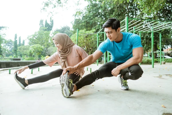Spor kıyafetli bir adam ve peçeli bir kız antrenmandan önce bacak esnetme hareketleri yapıyorlar. — Stok fotoğraf