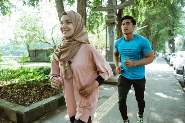 Un joven y una chica en un pañuelo para la cabeza haciendo jogging juntos cuando el ejercicio al aire libre —  Fotos de Stock