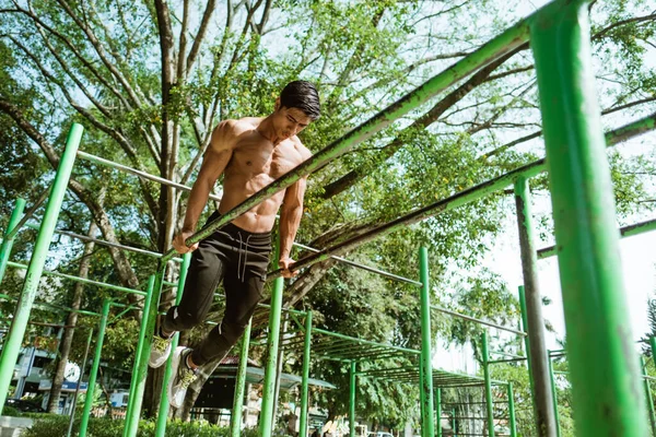 Um homem musculoso que faz pull ups para trabalhar seus músculos bíceps e tríceps — Fotografia de Stock