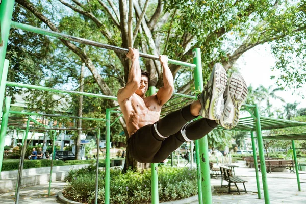 Um asiático muscular homem sem roupa fazendo L pull-up exercícios usando barra de ferro — Fotografia de Stock