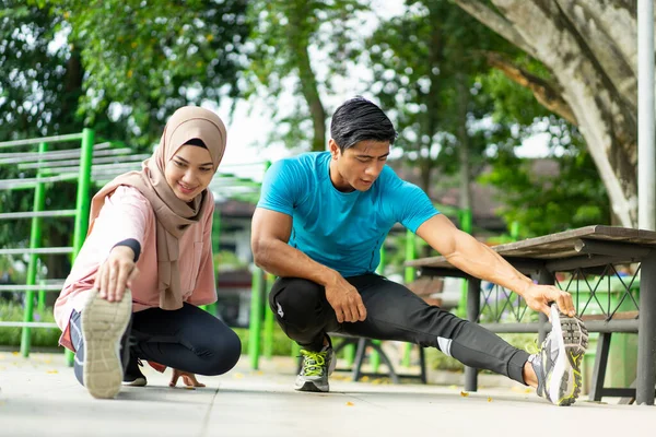 一个男人和一个穿着运动服披着面纱的女孩一起做腿部热身运动 — 图库照片