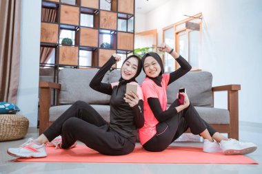 Spor kıyafetleri giyen iki kadın cep telefonu ekranını gördüklerinde şaşırmaktan mutlu olurlar.