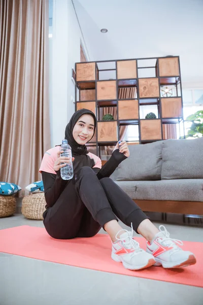Schuss von unten: Muslimin im Hijab-Turnanzug sitzt mit Trinkwasserflasche auf dem Boden — Stockfoto