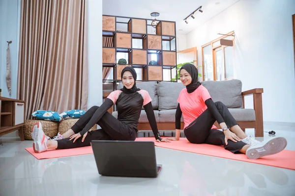 Dos mujeres que usan ropa deportiva de hijab se sientan en el suelo mientras calientan sus caderas — Foto de Stock