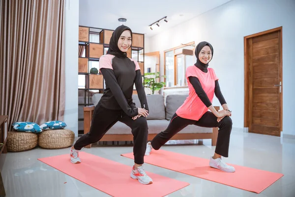 Δύο γυναίκες που φορούν μαντίλα χαμογελώντας ενώ κάνουν lunges κινήσεις κατά την άσκηση σε εσωτερικούς χώρους — Φωτογραφία Αρχείου