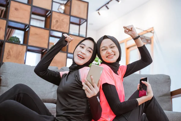 Gros plan de deux filles portant des vêtements de sport hijab sont heureux d'être surpris quand ils voient l'écran d'un téléphone portable — Photo