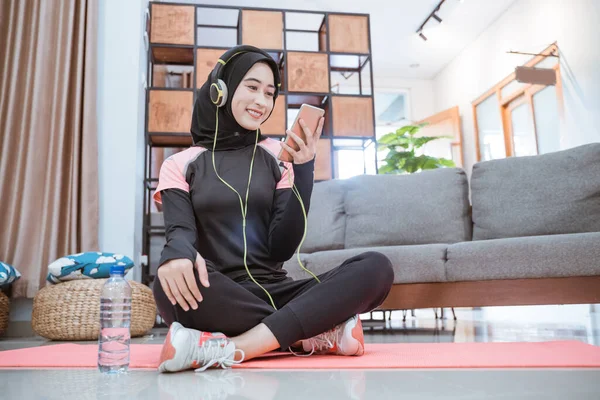 Eine Frau in Hijab-Sportkleidung mit Kopfhörer und Handy beim Musikhören — Stockfoto