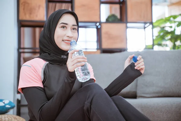 ヒジャーブのジムの衣装を着たイスラム教徒の女性のクローズアップは、飲料水ボトルを持って床に座っています — ストック写真