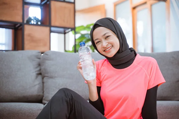 Asiático chica en un velo sportswear sonrisas mientras sosteniendo un beber botella mientras sentado en el suelo con un estera —  Fotos de Stock