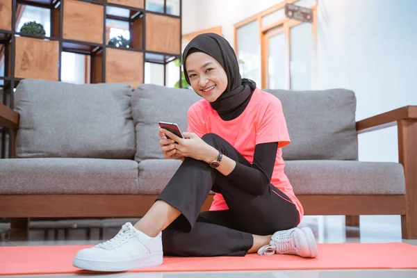 Une fille en hijab vêtements de sport sourit en regardant un téléphone portable assis sur le sol — Photo