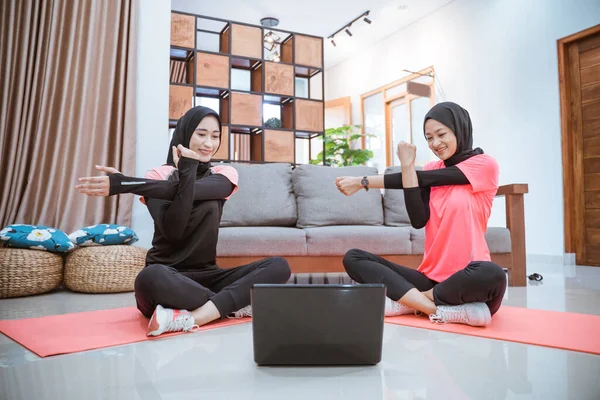 Dos mujeres musulmanas en ropa deportiva se sientan calentando con una mano sosteniendo la otra mano cuando una mano es jalada hacia un lado — Foto de Stock