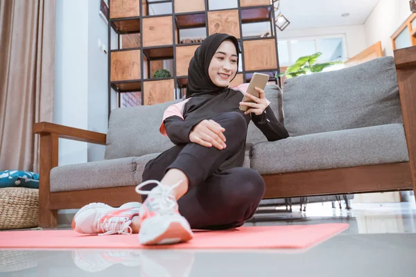 Une femme portant des vêtements de sport hijab à l'aide d'un téléphone portable assis détendu sur un matelas — Photo