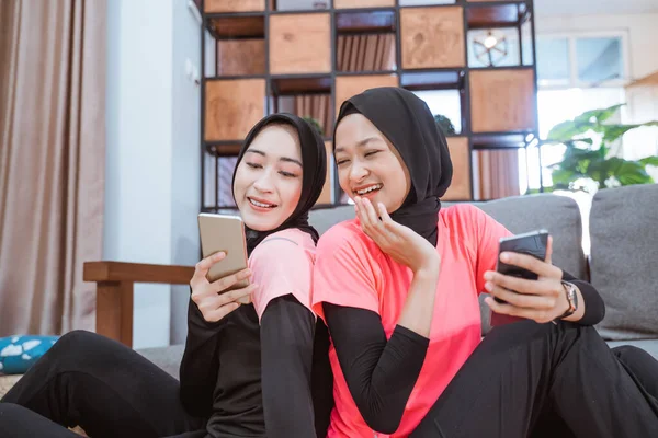 Twee vrouwen dragen hijab sportkleding lachen als ze kijken naar het scherm van een mobiele telefoon — Stockfoto