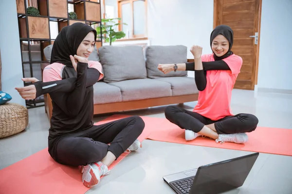 Deux femmes musulmanes dans des vêtements de sport s'assoient échauffant avec une main tenant l'autre main quand une main est tirée sur le côté — Photo
