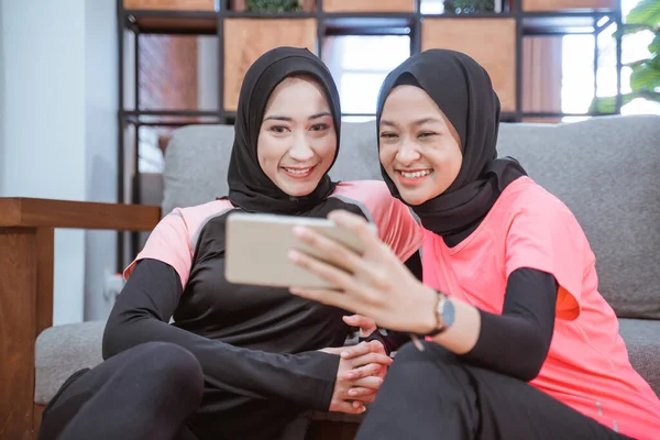 Dos mujeres que usan ropa deportiva de hijab sonriendo mientras toman selfies junto con un teléfono celular —  Fotos de Stock
