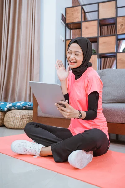 Une fille dans une tenue de gym voile avec un sourire regardant une tablette avec un geste de la main de dire bonjour — Photo