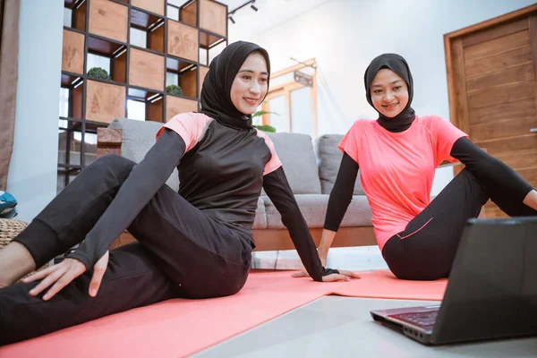 ヒジャーブのスポーツウェアを着た2人の女性が腰を上げながら床に座り — ストック写真