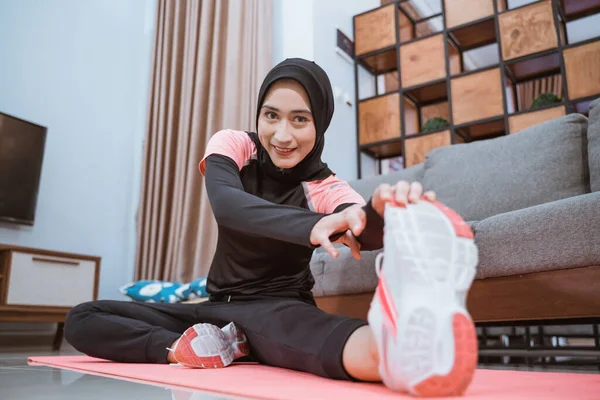 Primer plano de una mujer en hijab sportswear sonríe mientras está sentado estirando una pierna a un lado —  Fotos de Stock