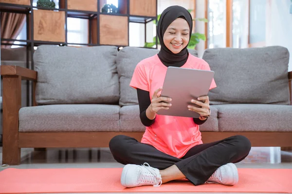 Una chica en un traje de gimnasio velo con una sonrisa mirando una tableta después del ejercicio en interiores — Foto de Stock