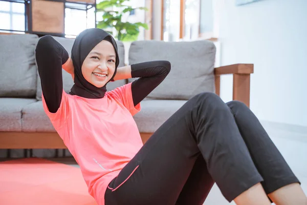 Nahaufnahme eines Mädchens im Hijab-Turnoutfit lächelt, während es ein Sit-up auf einer Matte macht — Stockfoto