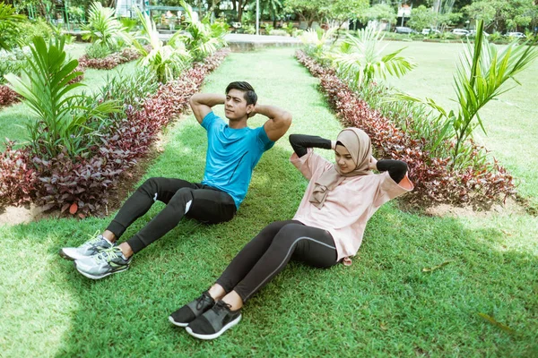 Un jeune homme et une fille dans un foulard faisant des mouvements pour entraîner les muscles abdominaux ensemble — Photo