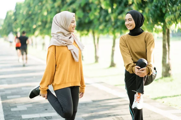 Twee tiener meisjes in sluier stretching hun been spieren door het opheffen en houden van de gebogen been met hun armen — Stockfoto