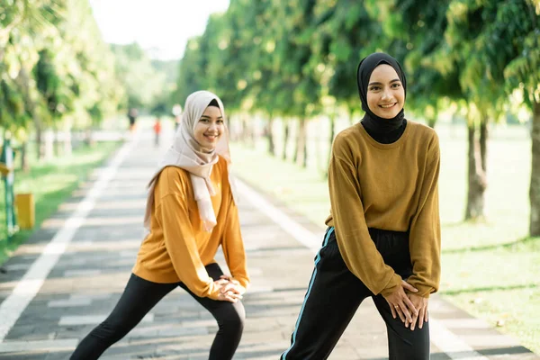 Two happy Muslim girls in headscarves do lunges before jogging — Stock Photo, Image