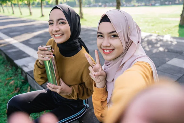 Dos chicas usando hijab sonriendo a una cámara de teléfono inteligente cuando selfie junto con el teléfono inteligente — Foto de Stock