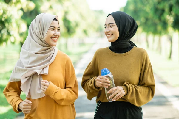 Dos chicas veladas disfrutan de hacer deportes al aire libre juntos mientras charlan y disfrutan de beber agua con una botella —  Fotos de Stock
