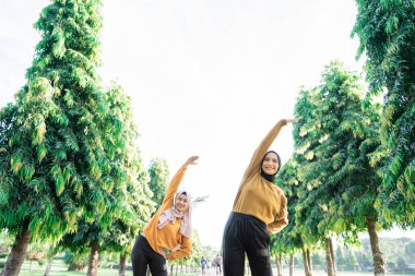 İki kızın peçesinin altından kollarını yukarı kaldırarak vücutlarını yana doğru eğerek kollarını gererler.