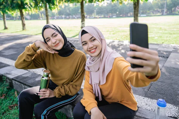 Twee meisjes dragen hijab glimlachen en het houden van een smartphone bij selfie samen met smartphone camera — Stockfoto