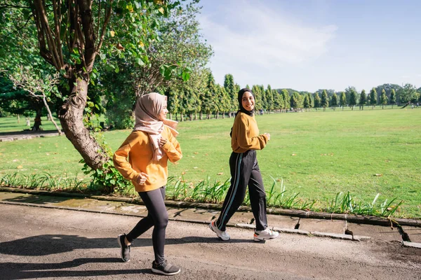 午後におしゃべりしながら一緒にジョギングを楽しむスカーフの2人のアジアの女の子 — ストック写真