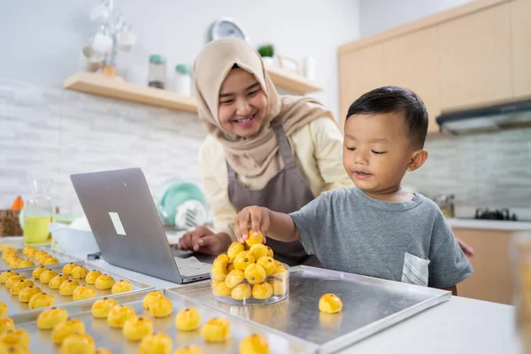 Ibu muslim melihat laptop sambil membuat kue dengan anaknya di dapur — Stok Foto