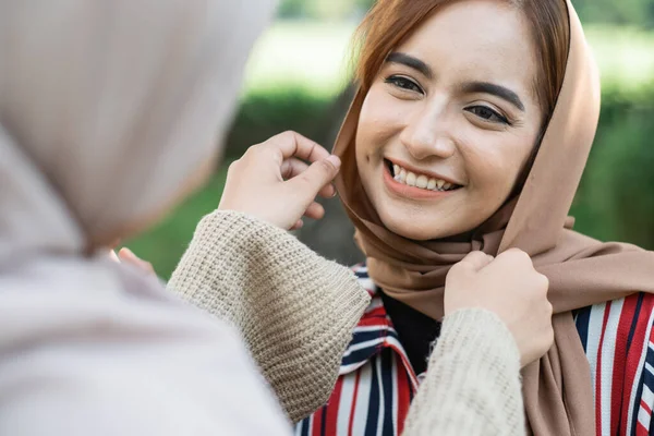 muslim asian woman fixing friend hijab while meeting outdoor