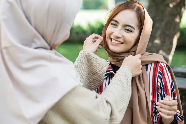 muslim asian woman fixing friend hijab while meeting outdoor