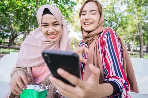 Мусульманка в платке встречается с друзьями и пользуется телефоном в парке — стоковое фото