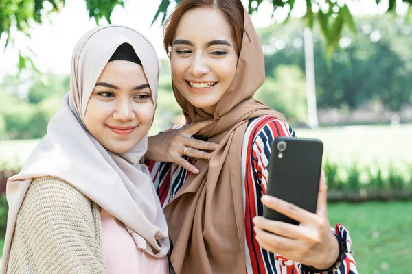 Musulmana mujer en la cabeza bufanda cumplir con amigos y el uso de teléfono en el parque — Foto de Stock