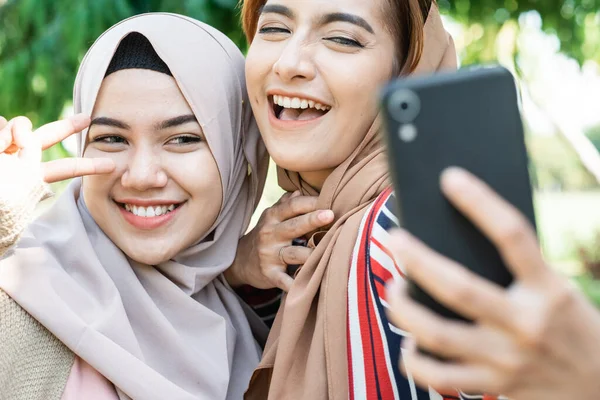 Mulher muçulmana na cabeça cachecol conhecer amigos e usando telefone no parque — Fotografia de Stock