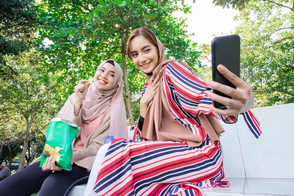 Moslim vrouw in hoofddoek ontmoeten vrienden en met behulp van de telefoon in het park — Stockfoto