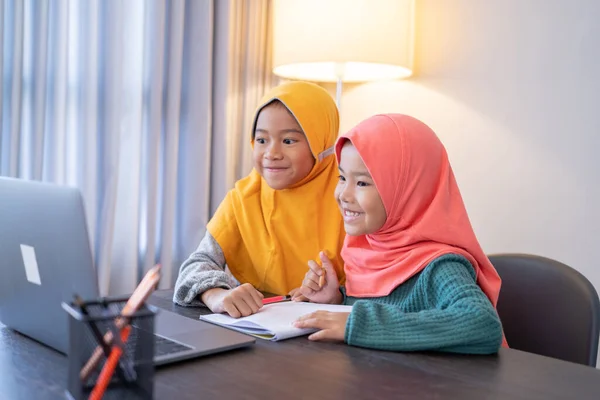 Niños musulmanes que usan pañuelo en la cabeza sonriendo mientras usan computadora portátil —  Fotos de Stock