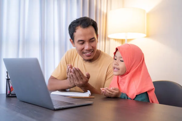 Müslüman ebeveyn ve kızı dizüstü bilgisayar kullanırken birlikte dua ediyorlar. — Stok fotoğraf