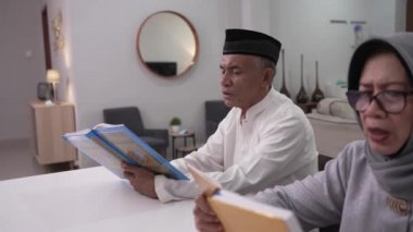 Müslüman kıdemli bir adam eşine oturma odasında Kur 'an veya Kuran okumayı öğretiyor.